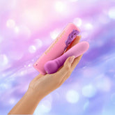 A hand holds the FemmeFunn Anniversary Ultra Bullet Orchid vibrator and its matching Femme Funn case against a soft, purple-blue bokeh background.
